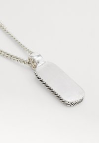 Colier din argint cu un pandantiv rectangular, având o textură periată și detalii intricate de margine gravate. Lanțul are un design torsionat.