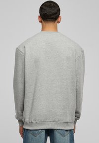 Sudadera gris con escote redondo, puños y dobladillo de canalé. Fabricada en una tela suave, presenta un corte ligeramente holgado.