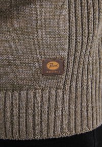 Primo piano di un maglione lavorato a maglia marrone-verde con orlo a coste e una etichetta in pelle marrone cucita con la scritta "Petrol Industries."