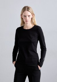 Sort langærmet top med rund halsudskæring og tætsiddende design. Har dekorationer langs ærmerne og en glat, blød tekstur.