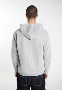 Šedá mikina s velkou kapucí. Na zadní straně má vyražený nápis "TUFF SKULL", žebrované manžety a uvolněný střih. Měkká textura, volnočasový design.