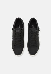 Black sneakers with lace-up design, rubber sole, and logo detail. Smooth texture with white accents on the sole and branding.