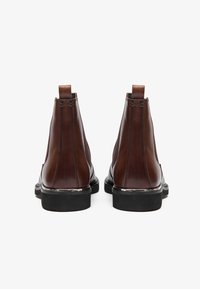 Botas Chelsea de cuero marrón con un acabado suave, paneles laterales elásticos y una suela de goma negra texturizada. Lengüetas en el talón para facilitar el calzado.