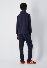 Chándal navy con cuello alto, mangas largas y rayas laterales. El material parece suave; incluye pantalones a juego y zapatillas rojas.