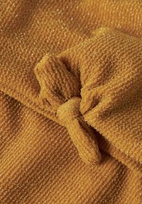 Tela de textura dorada con un patrón acanalado, que presenta un detalle en nudo. El material tiene un ligero brillo, lo que realza su interés visual.