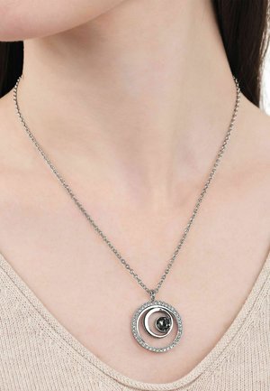 Zilveren ketting met twee concentrische cirkelvormige hangers, één bezet met kleine steentjes en een centrale grotere donkere edelsteen, gedragen om de hals.