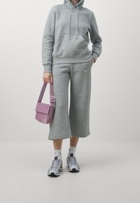 Grå sweatshirt med huva, kombinerad med matchande vida sweatpants. En metallic rosa axelväska och färgglada sneakers fulländar looken.