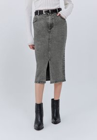 Gonna a matita in denim grigio con spacco frontale, vita alta e passanti per cintura, abbinata a stivaletti neri alla caviglia. Tessuto liscio e strutturato.