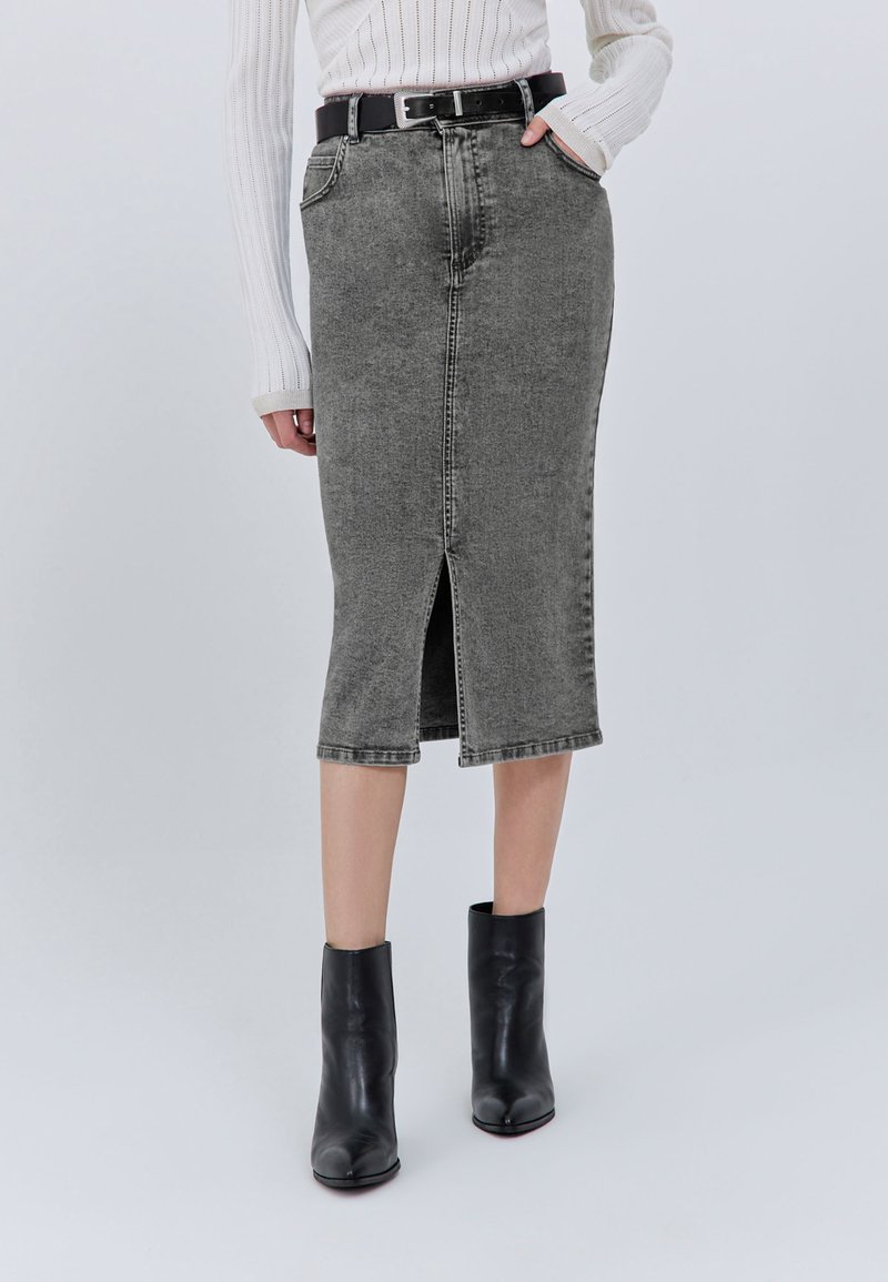 Gonna a matita in denim grigio con spacco frontale, vita alta e passanti per cintura, abbinata a stivaletti neri alla caviglia. Tessuto liscio e strutturato.