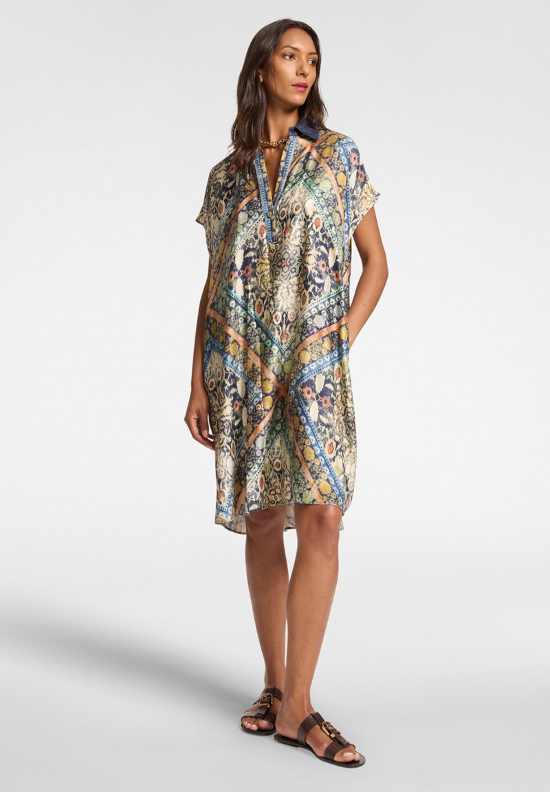 Kratký rukáv, šaty ke kolenům z lehké, vzorované tkaniny s geometrickými motivy v modré, zelené a oranžové barvě a předním rozparkem.