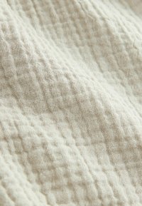 Tissu texturé beige clair avec un motif en grille, présentant une surface douce et tissée qui montre de subtiles variations d'épaisseur de tissage.