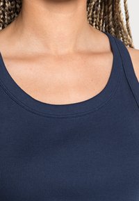 Marinblå ribbad linne med en bred, rund halsringning och tjocka axelband. Tyget ser mjukt och slätt ut med en nära passform.