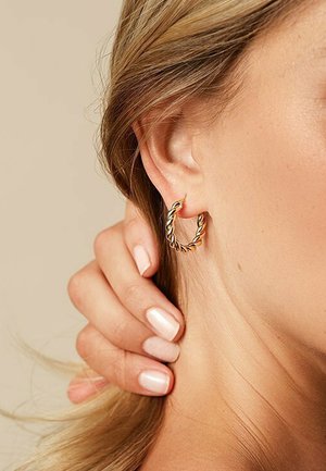 Gold hoop earrings with a twisted design, featuring a shiny surface and a small clasp. Worn on a model's ear against a neutral background.