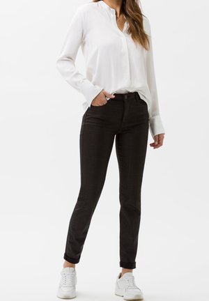 Pantalones negros con patrón y corte ajustado, que cuentan con un cierre de botón, bolsillos laterales y puños enrollados por encima del tobillo, combinados con una blusa blanca.