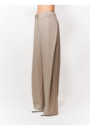 Beżowe spodnie o szerokich nogawkach z pętlami na pasek i zapięciem na guzik, noszone z białymi i czarnymi butami z zaostrzonym noskiem.