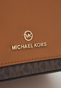 Brązowa skórzana torebka z złotym logo „MICHAEL KORS”, z ciemnym wzorzystym akcentem na dole. Gładka faktura i uporządkowany kształt.