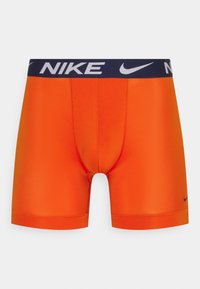 Narančaste atletske šortse s podržavajućim krojem. Sadrže tamnoplavi pojas s natpisom i logom "NIKE". Glatka, rastezljiva tkanina.