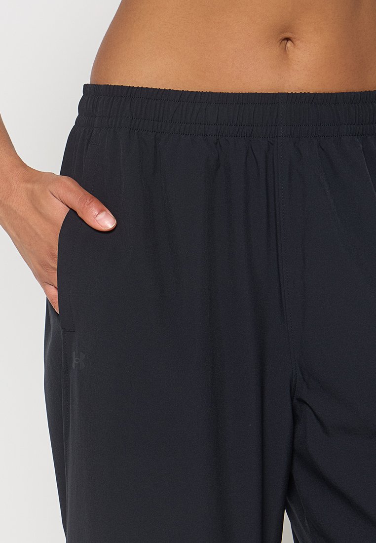 Pantalon de sport noir avec une taille élastique, des poches latérales et une texture lisse. Présente un petit logo sur la jambe inférieure.
