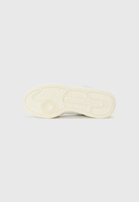 Gumeni đonovi tenisica u off-white boji, sa teksturiranim uzorcima i utorima za prianjanje. Minimalistički dizajn s detaljem logoa blizu pete.