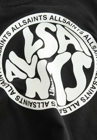 Črna bombažna majica z velikim belim grafičnim logotipom s stiliziranim besedilom in krožnimi oblikovnimi elementi. Mehka tekstura, priložnostna zasnova.