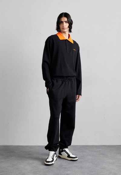 Sort langærmet polo med en lys orange krave, parret med sorte trækpants og sort-hvide sneakers. Enkel design, blødt stof.