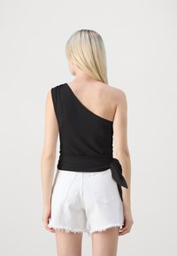 Svart, en-skulder topp med teksturert stoff og sideknutepunkt; kombinert med hvite denimshorts med frynsete kanter.