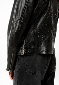Giubbotto di pelle nera con motivi a stella e borchie metalliche, vestibilità slim, polsini con zip e una fibbia regolabile in vita.