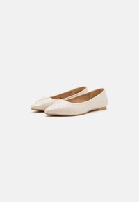 Cremfarbene Ballettschuhe mit spitzem Zeh, glänzender Oberfläche und schrägen Nähdetails an der Vorderseite. Flache Gummisohle.