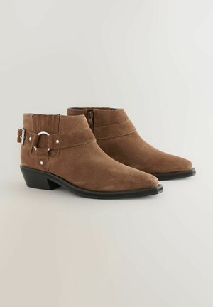 Stivaletti in suede marrone con punta appuntita, cerniera laterale e una cintura decorativa con una fibbia circolare in argento. Design con tacco basso e spesso.