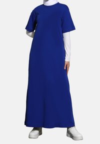 Maxi šaty v živé modré barvě; krátké rukávy, kulatý výstřih, vyrobené z měkké tkaniny; kombinované s bílými teniskami pro casual vzhled.