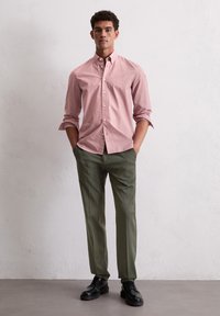 Rood-wit gestreept blouse, olijfgroene broek, zwarte veterschoenen. Gelaagd materiaal, nette pasvorm, opgerolde mouwen.