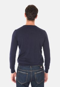 Maglione pullover blu navy, lavorato a maglia con una fine texture e polsini a costine, indossato con jeans blu scuro. Vista da dietro.