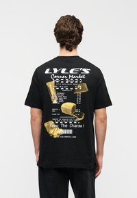 Μαύρο βαμβακερό T-shirt με μεγάλο γραφικό τύπωμα στην πλάτη, που μοιάζει με απόδειξη, με κίτρινα στοιχεία και κείμενο σε λευκό και χρυσό.