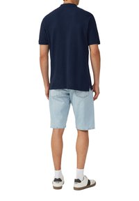 Marineblauwe polo met een gestructureerd patroon, gecombineerd met lichtblauwe spijkershorts. De shorts hebben een ontspannen pasvorm en zijn knielang. Witte sneakers.