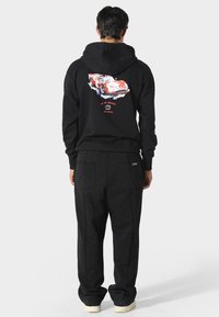 Sudadera negra con estampado gráfico de un coche en la parte trasera, combinada con pantalones de chándal negros a juego. Con un corte relajado, puños elásticos y bolsillos.