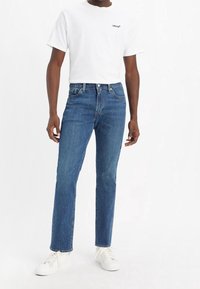 Niebieskie jeansy proste o klasycznym kroju, zestawione z białym t-shirtem Levi's z krótkim rękawem oraz białymi trampkami.