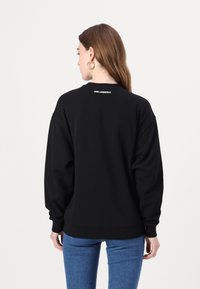 Svart sweatshirt med lös passform, ribbade ärmslut och rak fåll. Har logodetalj i vitt vid bakhalsen.