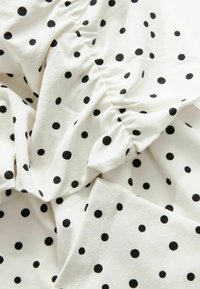 Tessuto bianco con pois neri, caratterizzato da una texture arricciata e contorni morbidi e scivolosi. Il motivo è distribuito in modo uniforme su tutta la superficie.
