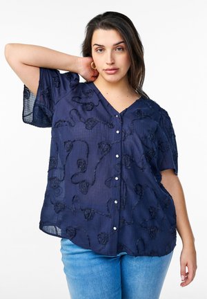 Blusa azul marino con escote en V, mangas cortas y bordado floral texturizado, con cierre de botones en el frente y tejido transparente.