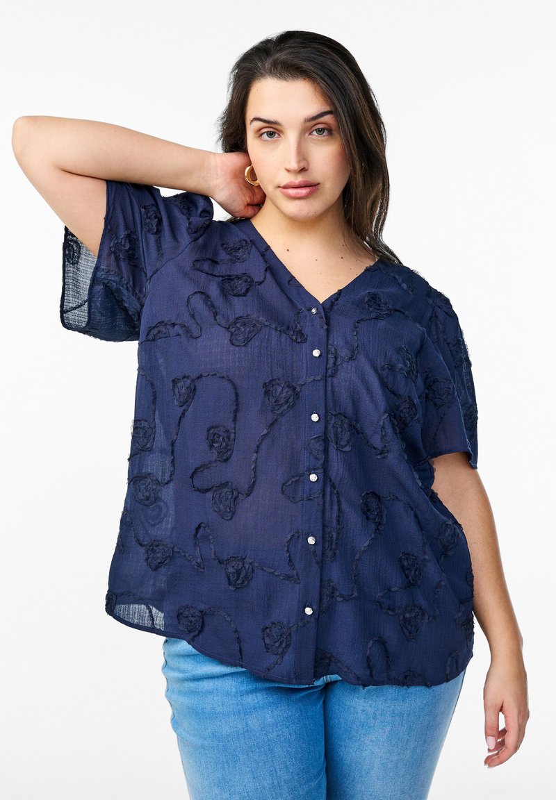 Blusa blu navy con scollo a V, maniche corte e ricamo floreale testurizzato, con chiusura a bottoni e tessuto trasparente.