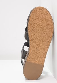 Black leather sandal with cork sole, featuring a textured bottom for grip and three wide straps for support.