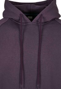 Paarse hoodie van een gestructureerde stof, met een trekkoordkap, ribgebreide manchetten en een kangoeroezak. Merklabel zichtbaar aan de binnenkant.