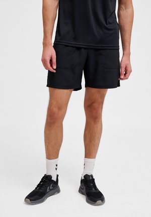 Zwarte sportshorts met een gladde textuur en zakken, gecombineerd met zwarte sneakers en witte sokken met een chevronpatroon.
