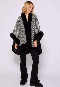 Czarna i biała peleryna w pepitkę z miękkim czarnym futrzanym kołnierzem i obszyciem. Luźny krój, sięgająca do kolan, noszona na czarnych spodniach i botkach.