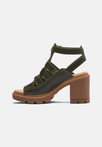 Sandale à brides vert olive avec un talon bloc marron épais et une semelle robuste, équipée d'une bride cheville avec fermeture à scratch.