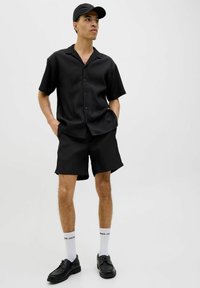 Sort sæt bestående af kortærmet skjorte og shorts med en lodret stribemønster. Bæres med sorte sko og hvide sokker. Komplementeres med en sort kasket.