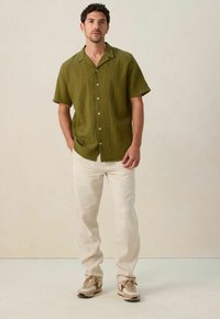 Olijfgroen overhemd met korte mouwen en een gestructureerde stof, gecombineerd met lichtbeige broek en bruine sneakers.