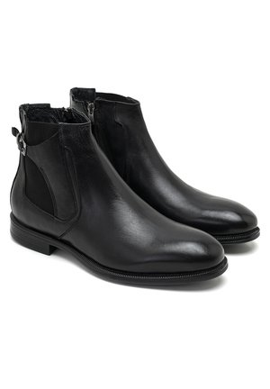 Bottines en cuir noir avec une finition lisse, des panneaux latéraux élastiques et une fermeture éclair sur le côté. Présentent des accents en métal argenté et un petit talon.