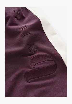 Material sportiv burgundy cu margini albe contrastante; prezintă detalii în relief cu inscripția "by" și numărul "0" într-un finisaj texturat. Textură moale și netedă.