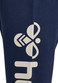 Marineblauwe katoen joggers met een groot wit logo en tekstontwerp. De stof heeft een gladde textuur en een strakke pasvorm.